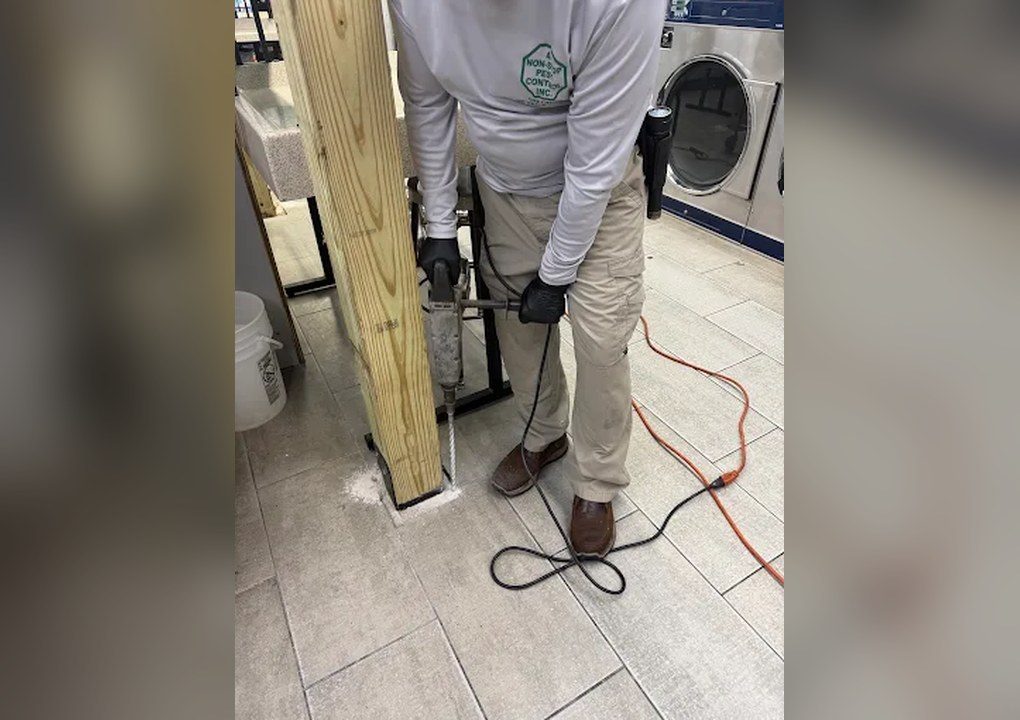 A Non-Stop technician drilling the floor next to a wood post for a termite treatment